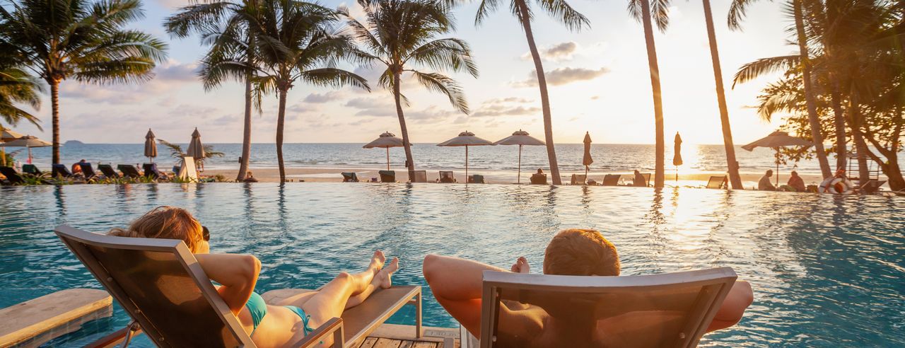 Ein Pärchen entspannt sich auf Liegestühlen am Pool mit Blick auf das Meer und die Palmen.