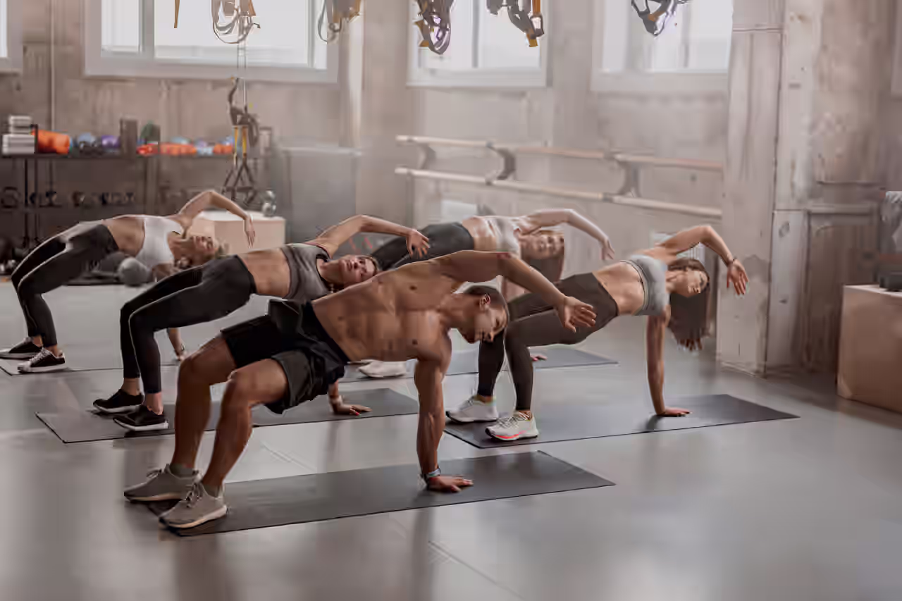 Gruppe von sehr sportlichen Menschen beim Training auf Matten in einem Fitness-Studio