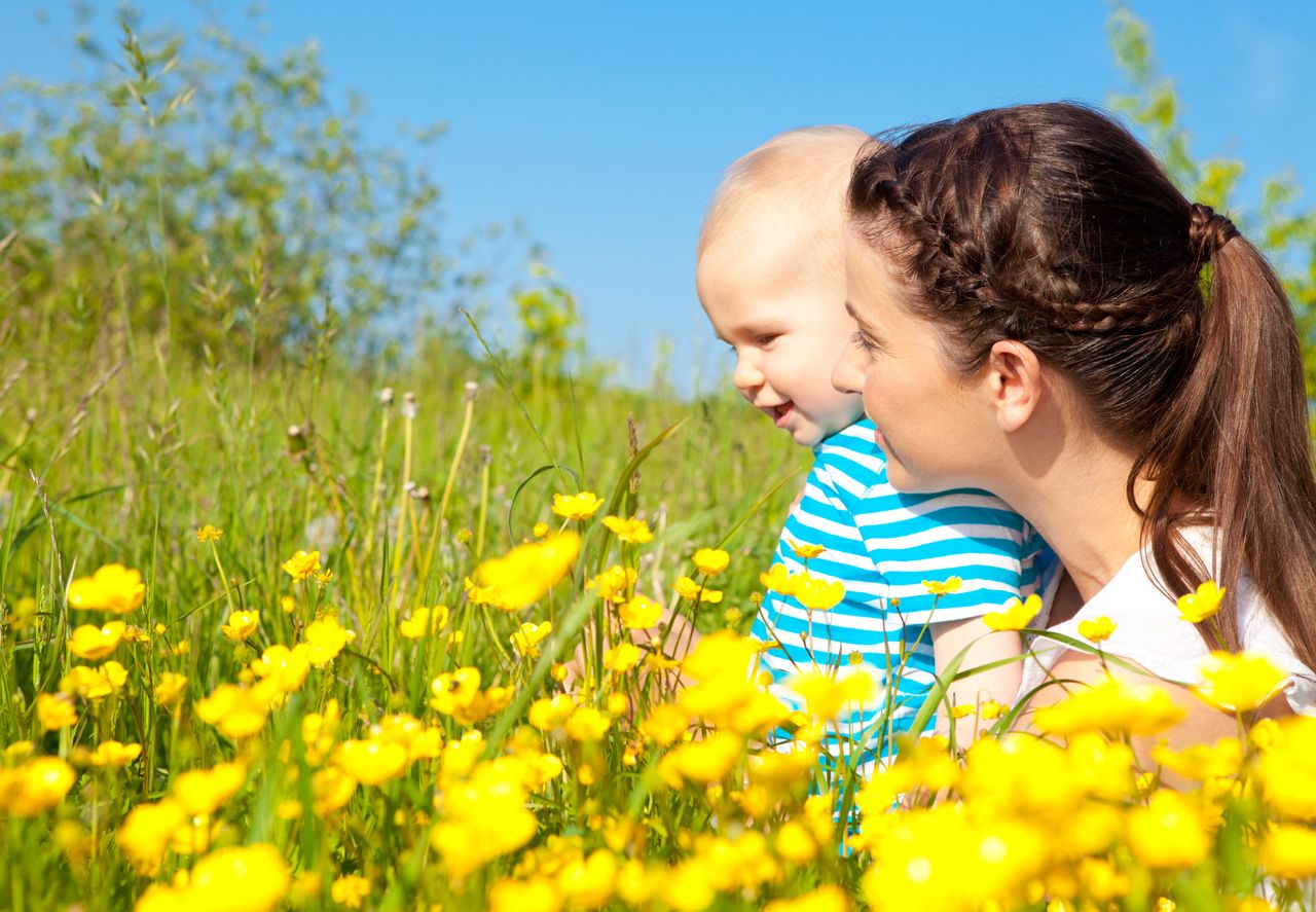 Eine Frau sitzt mit ihrem Kleinkind auf einer Blumenwiese