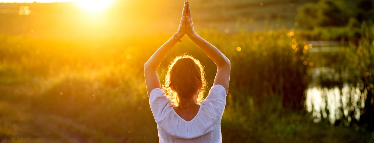 Frau macht Sonnengruß auf einer Wiese bei einem Yoga Wochenende in Österreich