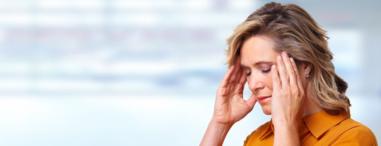 Woman in orange top holding her temples with her eyes closed as if suffering from a headache or stress.