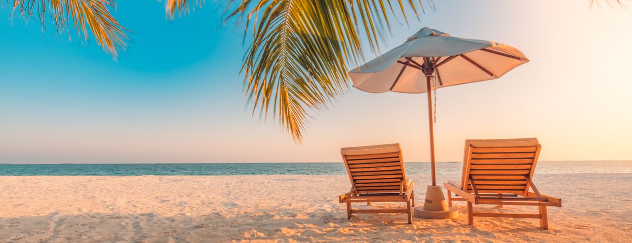 Twee strandstoelen staan op het witte zandstrand, palmbladeren en een parasol
