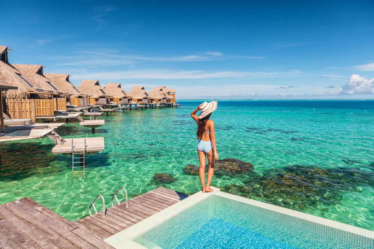 Eine Frau steht am Rande eines Pools eines Bungalows auf Stelzen über dem Meer