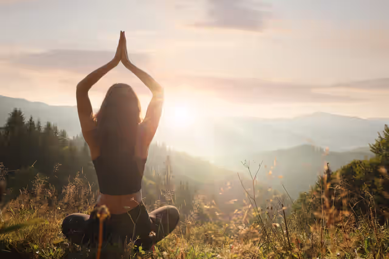 Frau macht bei Sonnenaufgang Yoga auf einer Wiese mit Blick auf die Berge