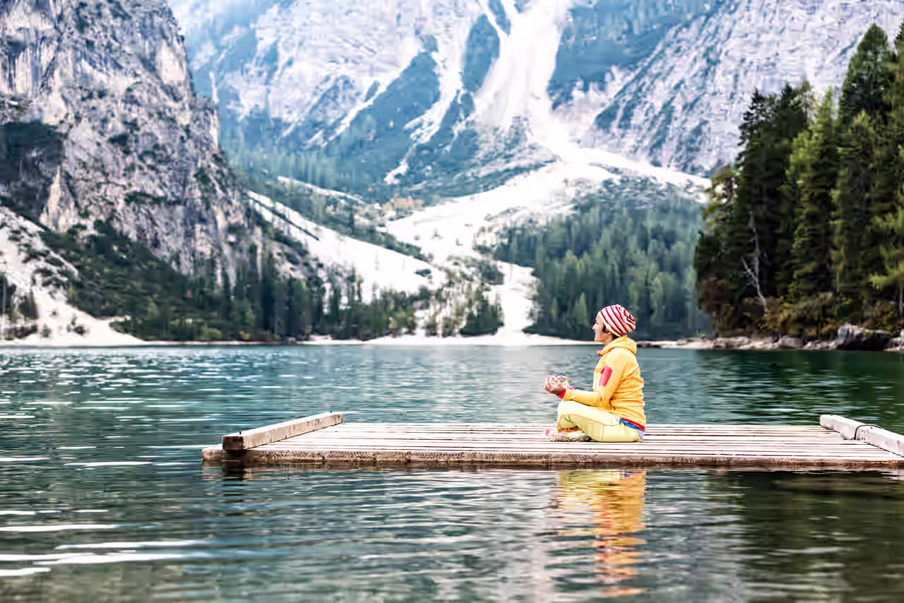Eine Frau praktiziert Yoga auf einem Steg auf einem See in Südtirol mit den Bergen im Hintergrund.