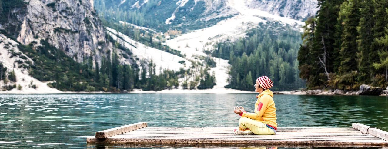 Eine Frau praktiziert Yoga auf einem Steg auf einem See in Südtirol mit den Bergen im Hintergrund.