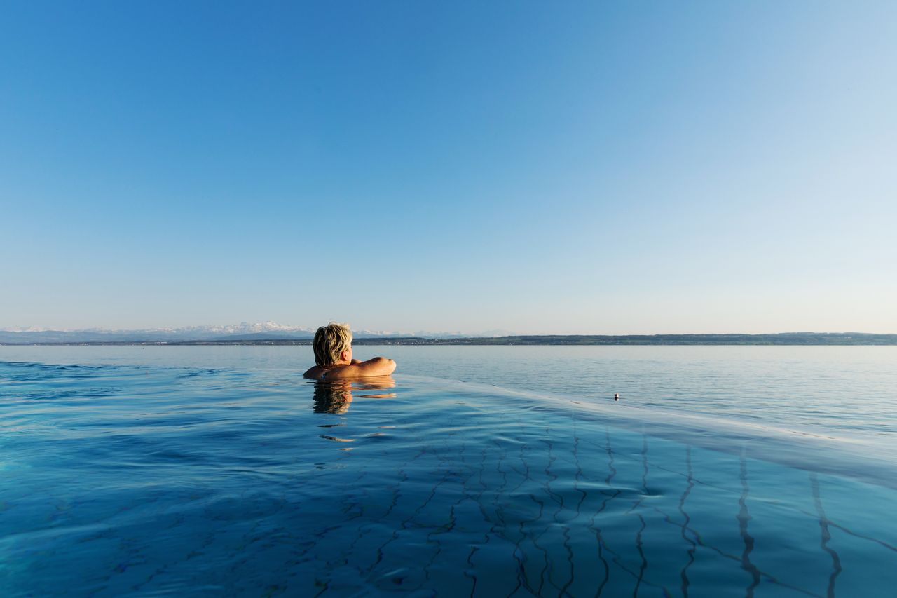Eine Frau im Infinity Pool mit Blick auf den Bodensee