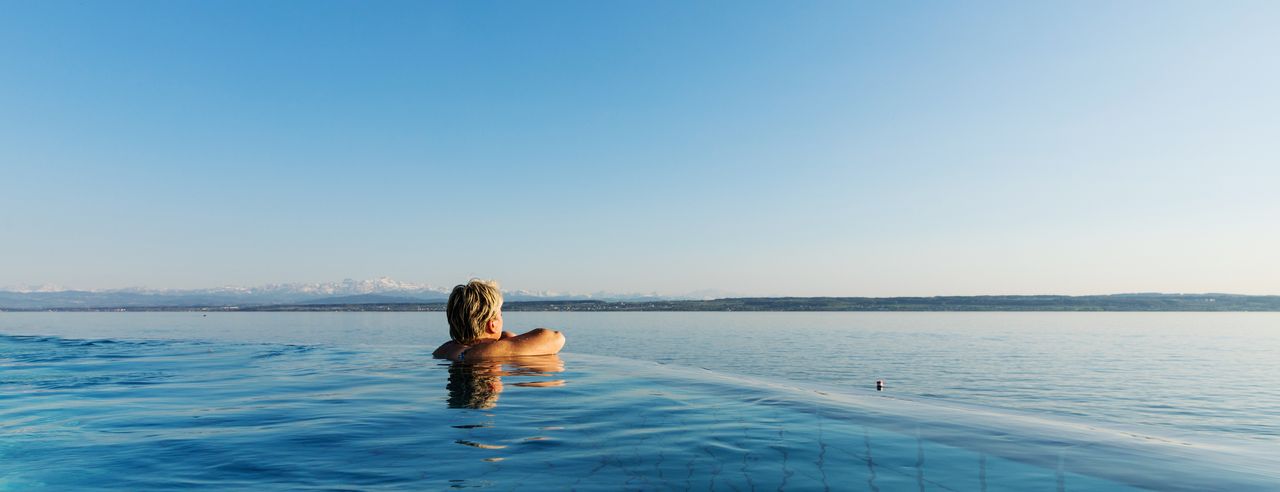 Eine Frau im Infinity Pool mit Blick auf den Bodensee