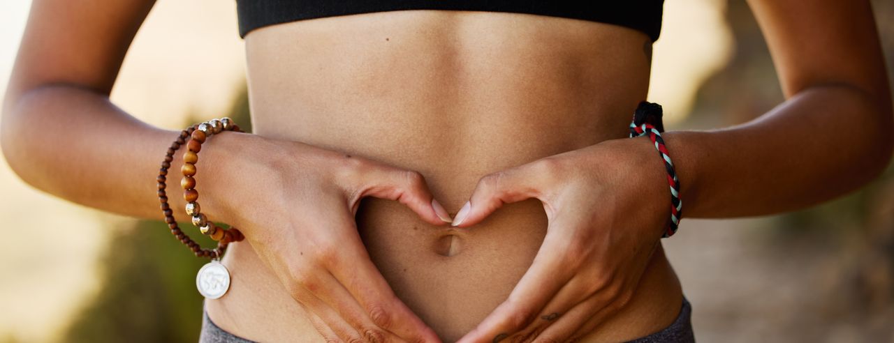 A woman forms a heart in front of her stomach, symbolizing the effect of meditation on healthy intestinal flora