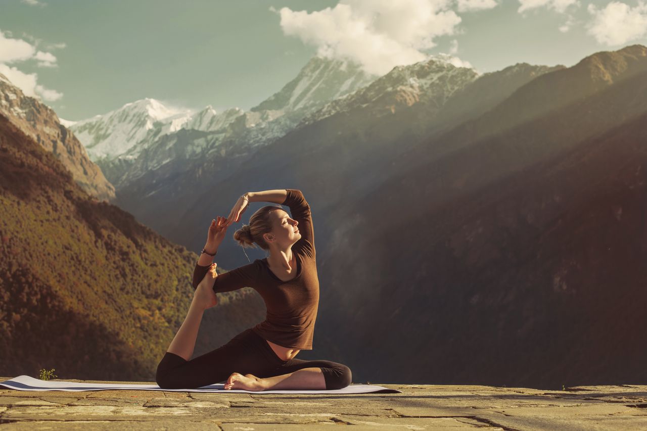 Eine Frau steht inmitten einer Berglandschaft und macht eine Yoga-Pose.