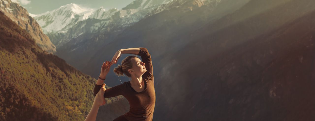 Eine Frau steht inmitten einer Berglandschaft und macht eine Yoga-Pose.