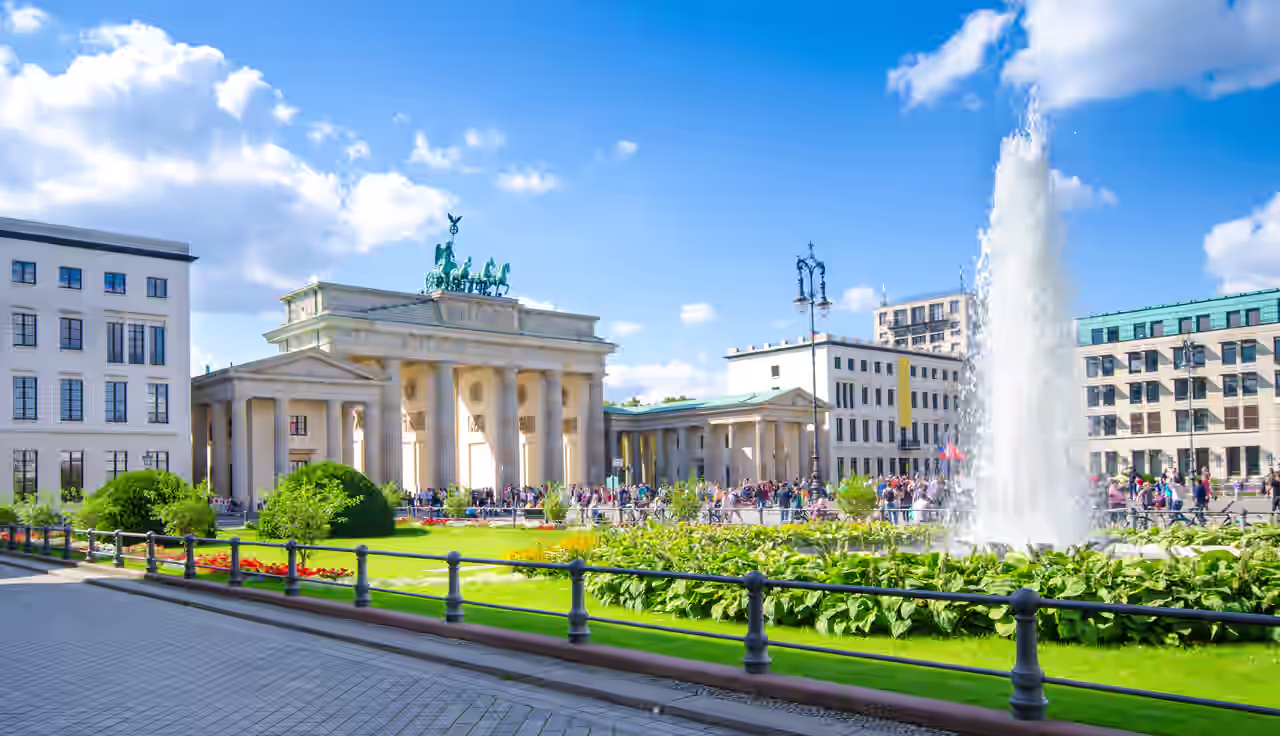 Brandenburger Tor hinter Grünanlage mit Fontäne im Sonnenschein beim Wellness Wochenende in Berlin